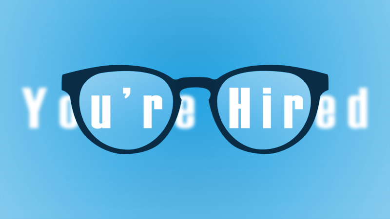 The words "you're hired" viewed through glasses. Everything outside the lens is blurry.